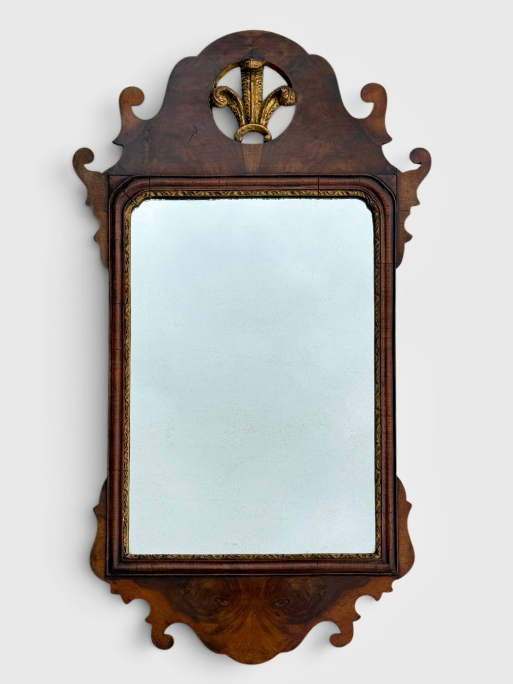 An 18th-century Georgian wall mirror featuring a carved walnut fretwork frame with a central gilded plume motif at the top.