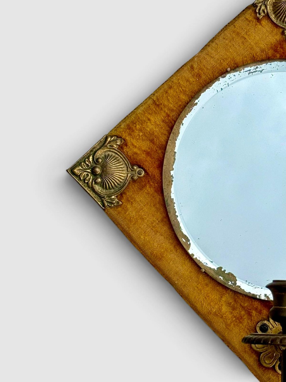 A diamond-shaped wall mirror featuring a mustard yellow velvet frame with decorative brass corner mounts, a central round bevelled glass mirror, and an integrated brass candle sconce at the lower vertex. View II