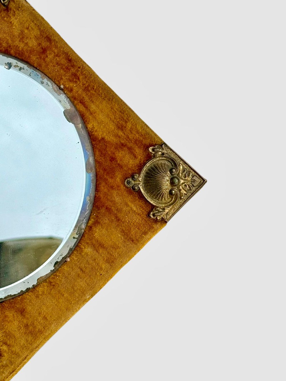A diamond-shaped wall mirror featuring a mustard yellow velvet frame with decorative brass corner mounts, a central round bevelled glass mirror, and an integrated brass candle sconce at the lower vertex. View VIII