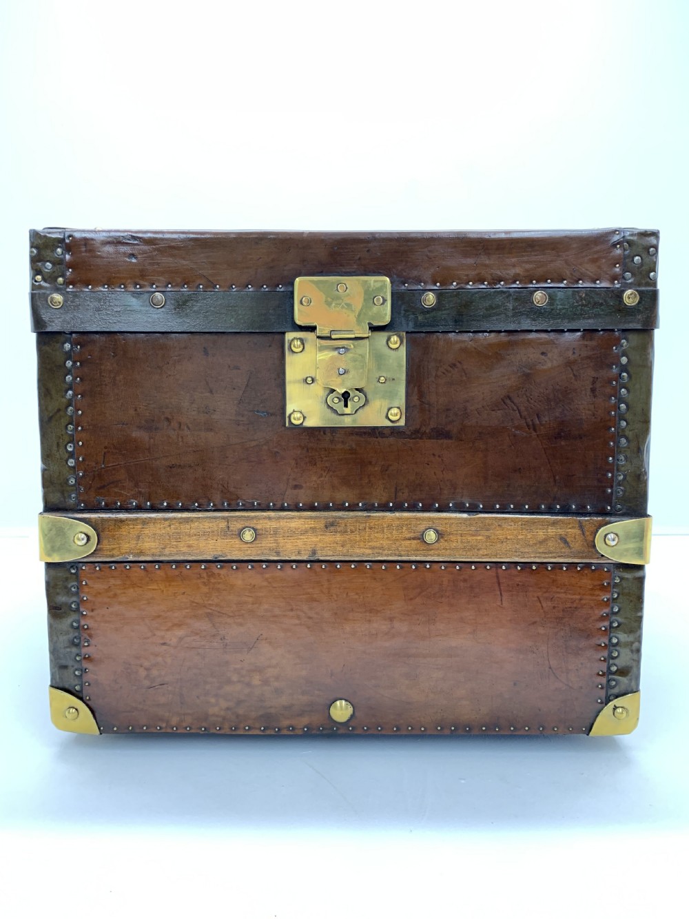 A dark brown antique leather steamer trunk featuring brass hardware, riveted metal stud trim, and wooden reinforcement bands.