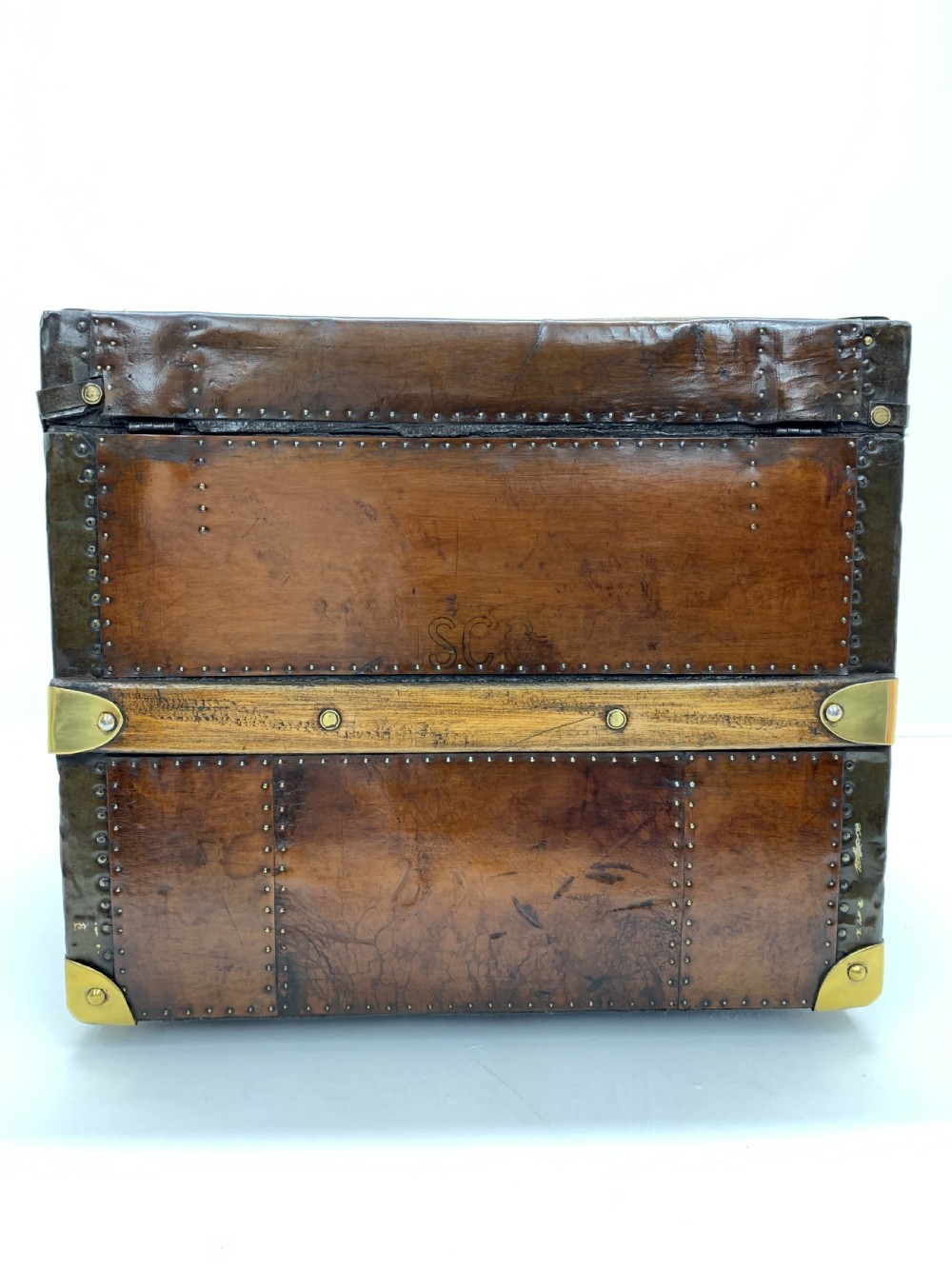 A dark brown antique leather steamer trunk featuring brass hardware, riveted metal stud trim, and wooden reinforcement bands. View IV