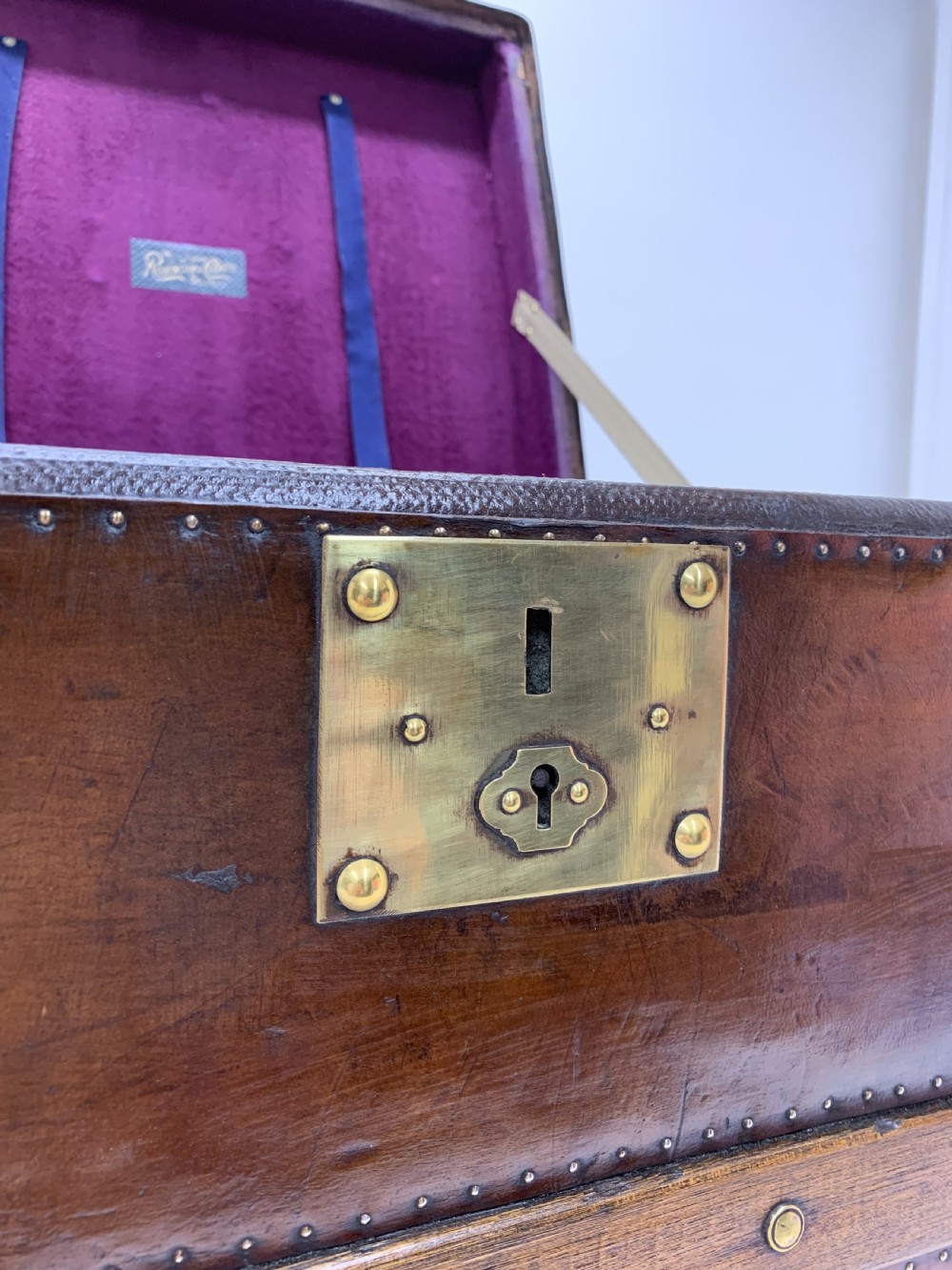 A dark brown antique leather steamer trunk featuring brass hardware, riveted metal stud trim, and wooden reinforcement bands. View XII