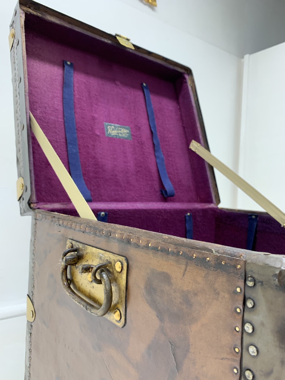 A dark brown antique leather steamer trunk featuring brass hardware, riveted metal stud trim, and wooden reinforcement bands. View XIII