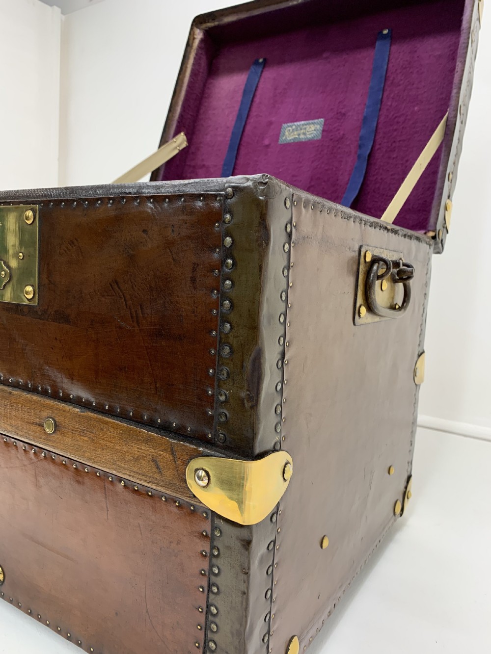 A dark brown antique leather steamer trunk featuring brass hardware, riveted metal stud trim, and wooden reinforcement bands. View XIV