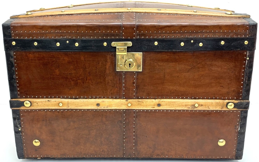 An antique leather-bound dome top steamer trunk with brass studs, wooden slats, and a central brass lock mechanism.