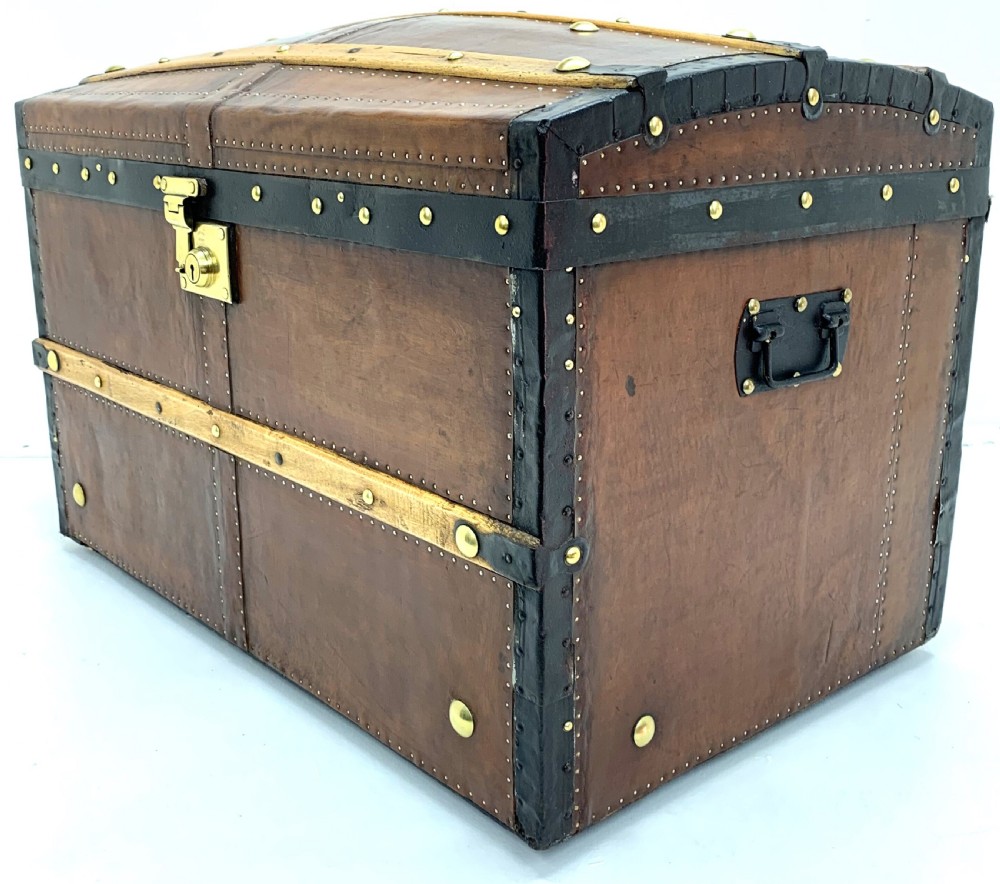 An antique leather-bound dome top steamer trunk with brass studs, wooden slats, and a central brass lock mechanism. View II