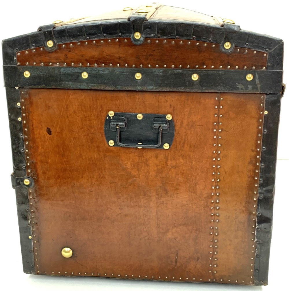 An antique leather-bound dome top steamer trunk with brass studs, wooden slats, and a central brass lock mechanism. View III