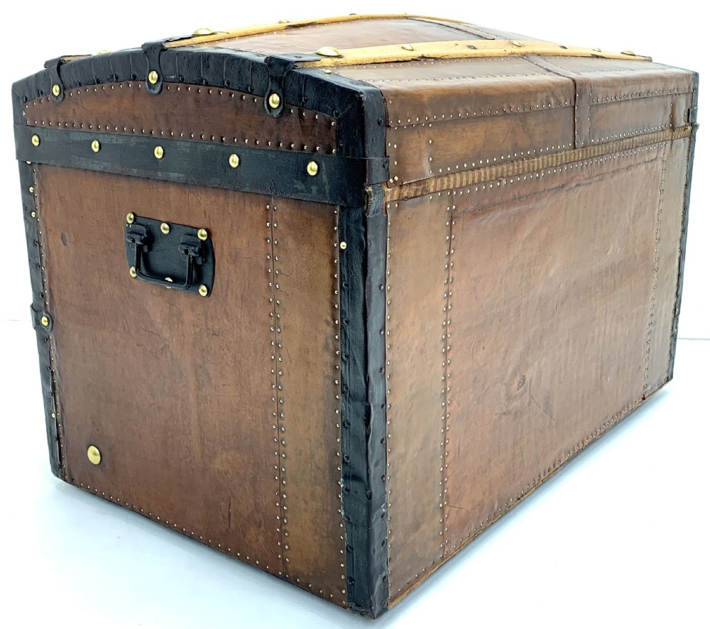An antique leather-bound dome top steamer trunk with brass studs, wooden slats, and a central brass lock mechanism. View IV