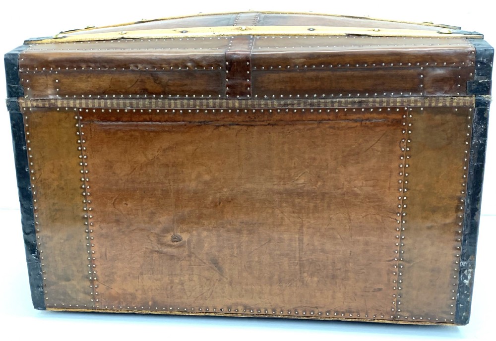 An antique leather-bound dome top steamer trunk with brass studs, wooden slats, and a central brass lock mechanism. View V