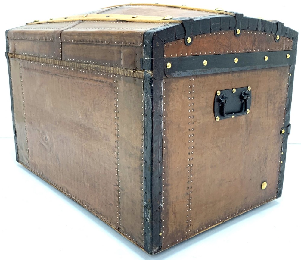 An antique leather-bound dome top steamer trunk with brass studs, wooden slats, and a central brass lock mechanism. View VI