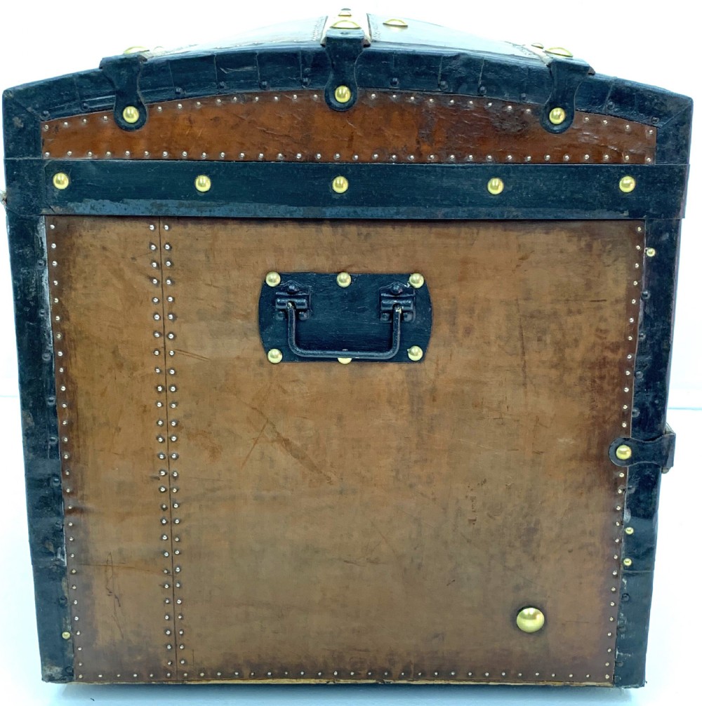 An antique leather-bound dome top steamer trunk with brass studs, wooden slats, and a central brass lock mechanism. View VII