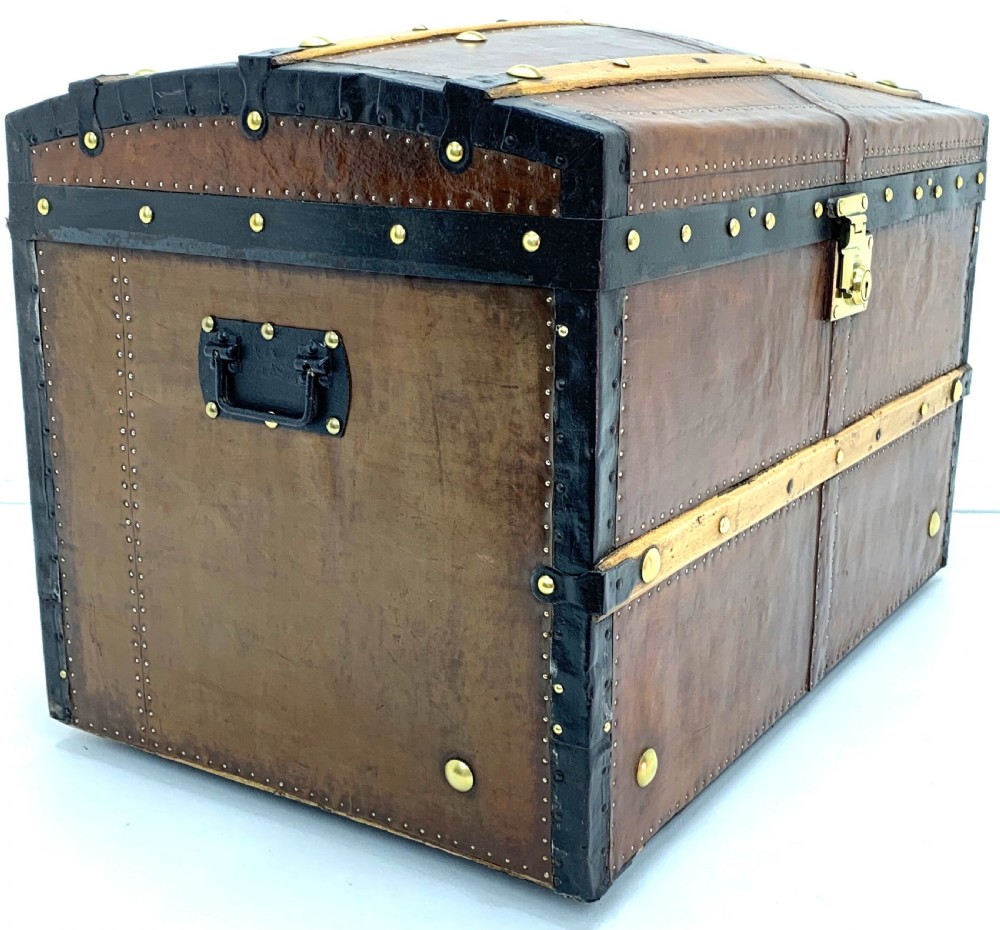 An antique leather-bound dome top steamer trunk with brass studs, wooden slats, and a central brass lock mechanism. View VIII