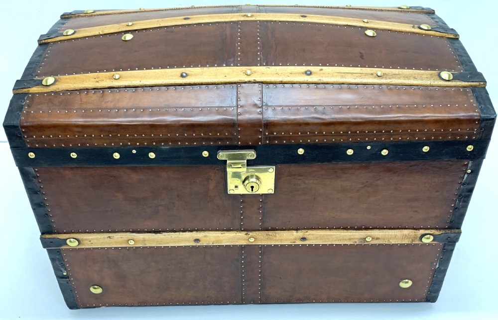 An antique leather-bound dome top steamer trunk with brass studs, wooden slats, and a central brass lock mechanism. View IX