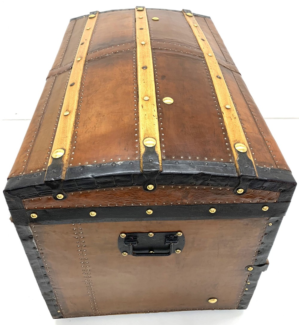 An antique leather-bound dome top steamer trunk with brass studs, wooden slats, and a central brass lock mechanism. View XI
