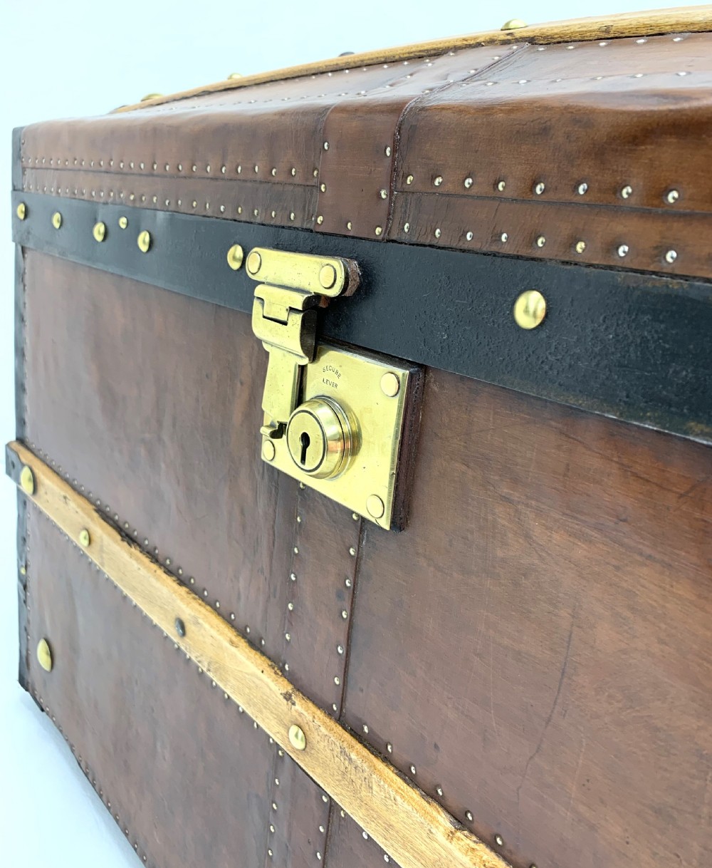 An antique leather-bound dome top steamer trunk with brass studs, wooden slats, and a central brass lock mechanism. View XII