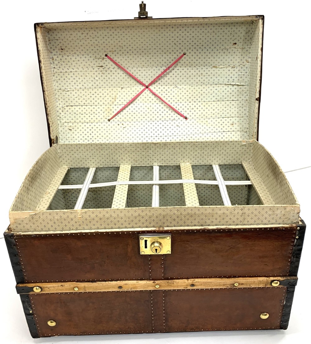 An antique leather-bound dome top steamer trunk with brass studs, wooden slats, and a central brass lock mechanism. View XIV