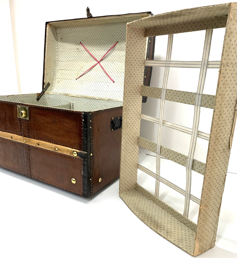 An antique leather-bound dome top steamer trunk with brass studs, wooden slats, and a central brass lock mechanism. View XVII