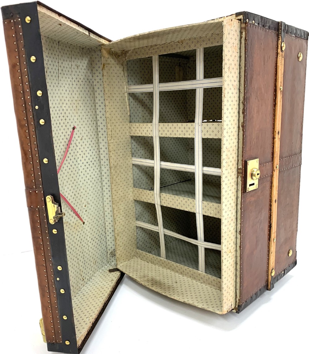 An antique leather-bound dome top steamer trunk with brass studs, wooden slats, and a central brass lock mechanism. View XIX