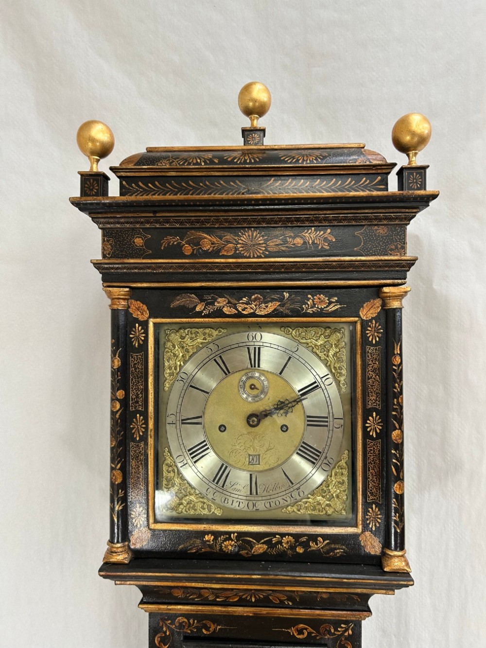 A tall black japanned longcase clock featuring gold chinoiserie motifs, turned hood columns, three gilded ball finials, and a brass dial with a silvered chapter ring. View II