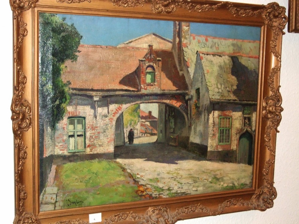 An oil painting depicting a European village courtyard with a brick archway, gabled buildings, and a distant figure, set within an ornate swept gilt frame.
