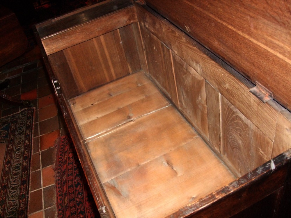 An 18th-century dark oak mule chest featuring a hinged top lid, three fielded panels across the front facade, two base drawers with brass handles, and bracket feet. View III