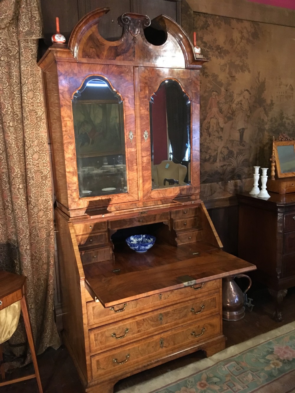 A George I walnut bureau bookcase featuring an arched pediment, two mirrored doors on the upper cabinet, and a sloping fall-front desk over three long drawers.