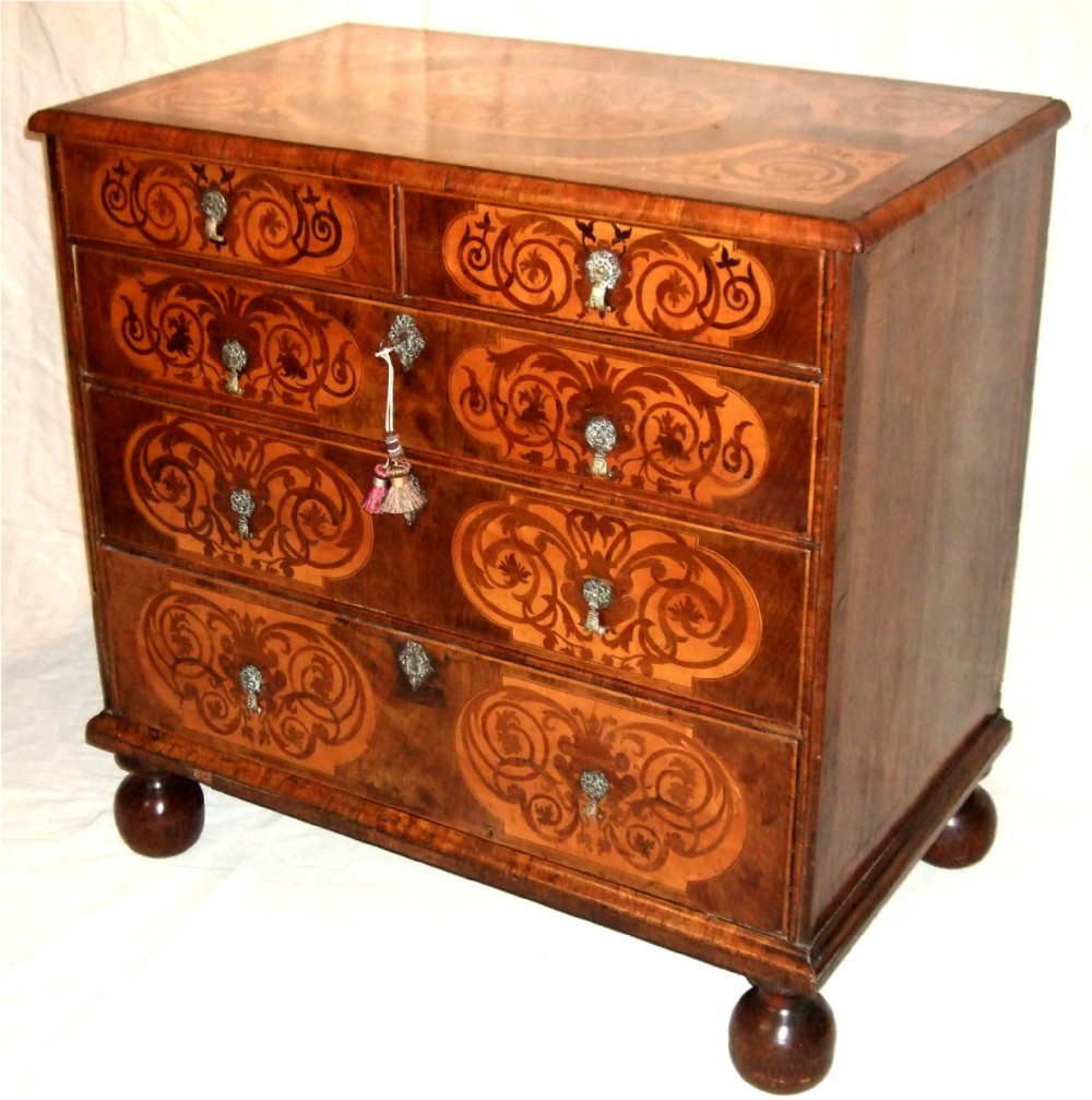 A William and Mary walnut chest of drawers featuring ornate floral marquetry inlays, brass drop handles, and turned bun feet.