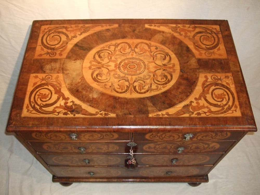 A William and Mary walnut chest of drawers featuring ornate floral marquetry inlays, brass drop handles, and turned bun feet. View II