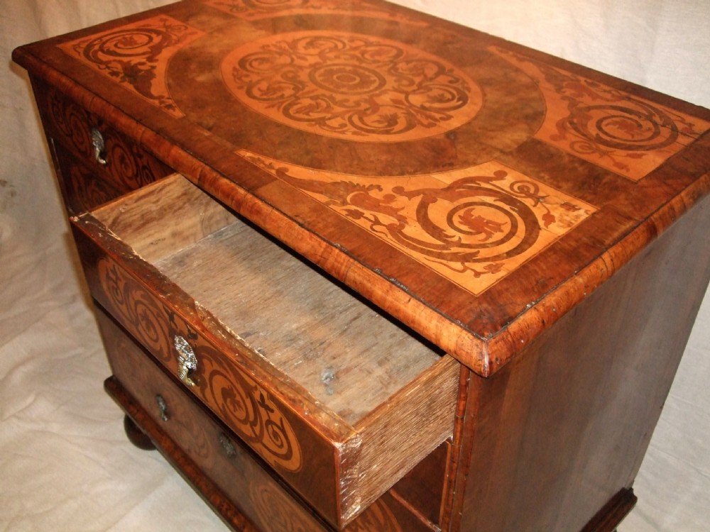 A William and Mary walnut chest of drawers featuring ornate floral marquetry inlays, brass drop handles, and turned bun feet. View VI