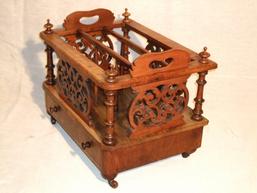A Victorian walnut music Canterbury featuring open compartments with carved fretwork dividers, corner turned pillars with finials, a lower drawer with twin knobs, and castor feet. View II