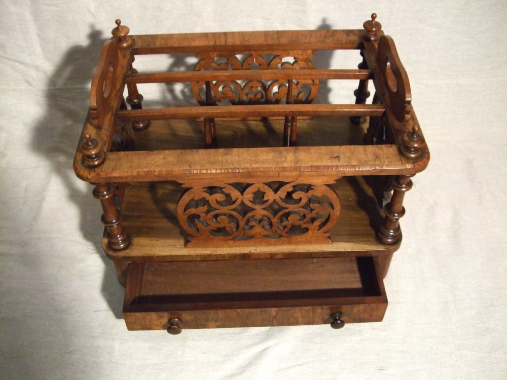 A Victorian walnut music Canterbury featuring open compartments with carved fretwork dividers, corner turned pillars with finials, a lower drawer with twin knobs, and castor feet. View III