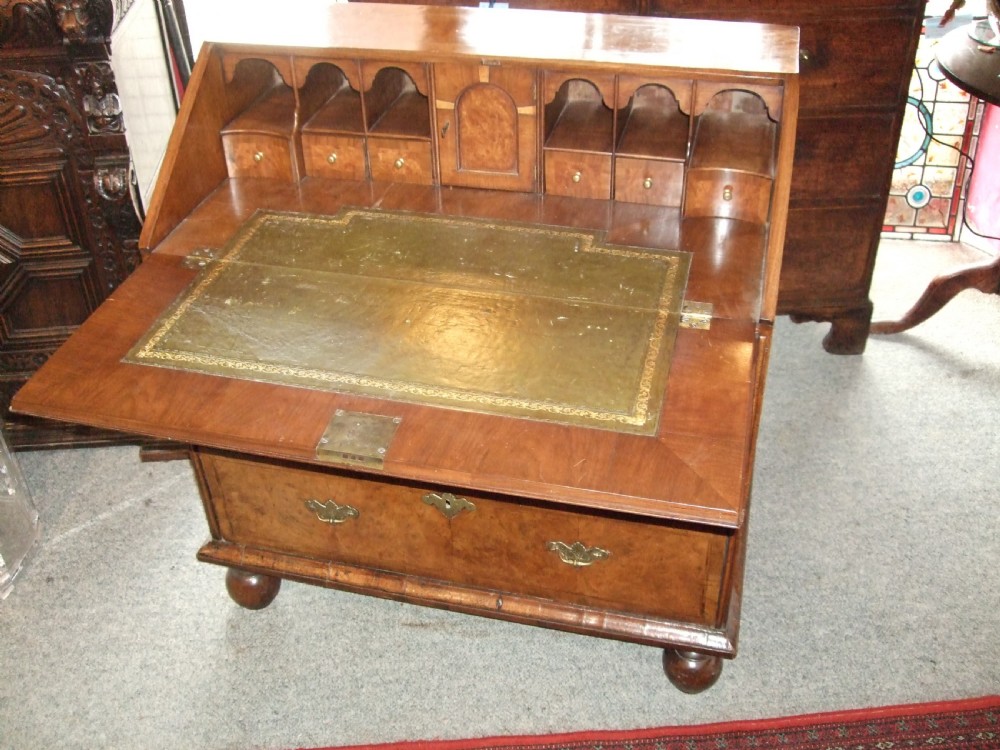 An early 18th-century burr walnut bureau featuring a sloping fall-front lid, engraved brass escutcheons, graduated drawers, and turned bun feet. View II