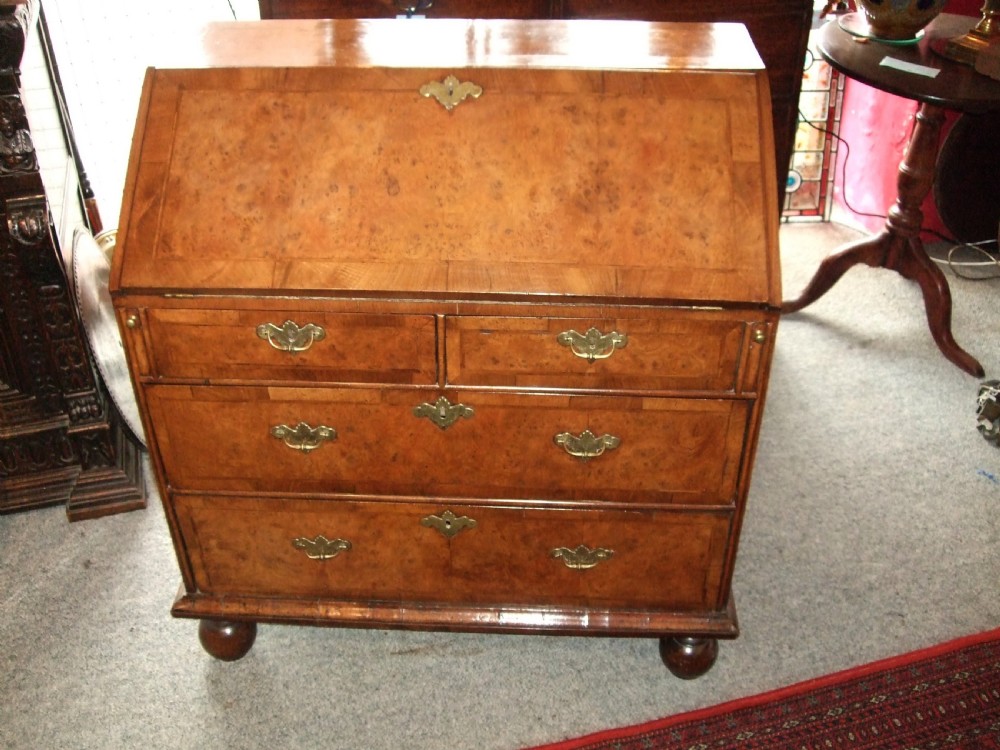An early 18th-century burr walnut bureau featuring a sloping fall-front lid, engraved brass escutcheons, graduated drawers, and turned bun feet. View III