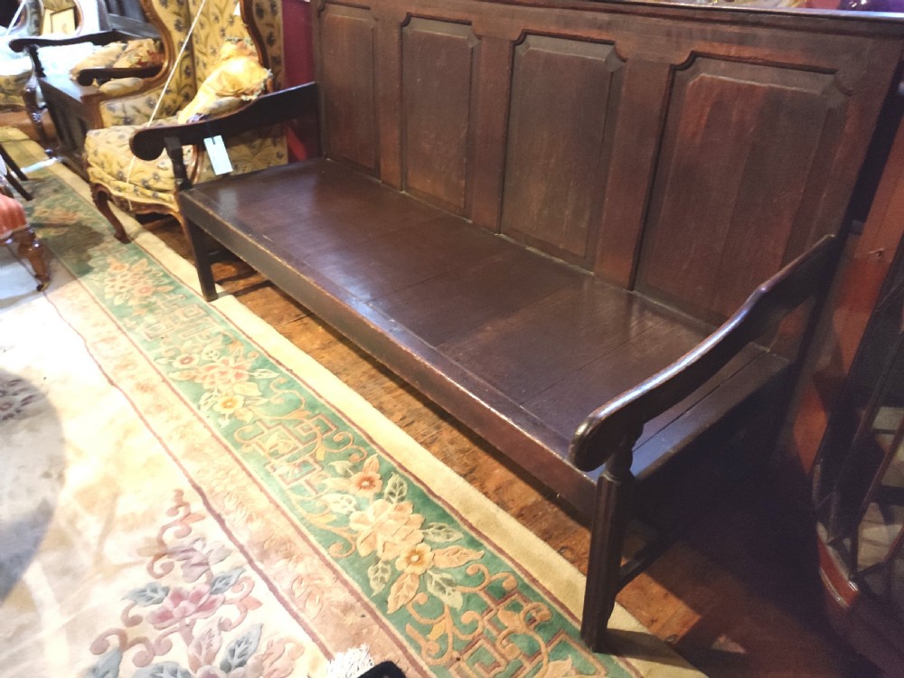 An 18th-century dark oak panelled settle with four fielded back panels and shaped side armrests. View II
