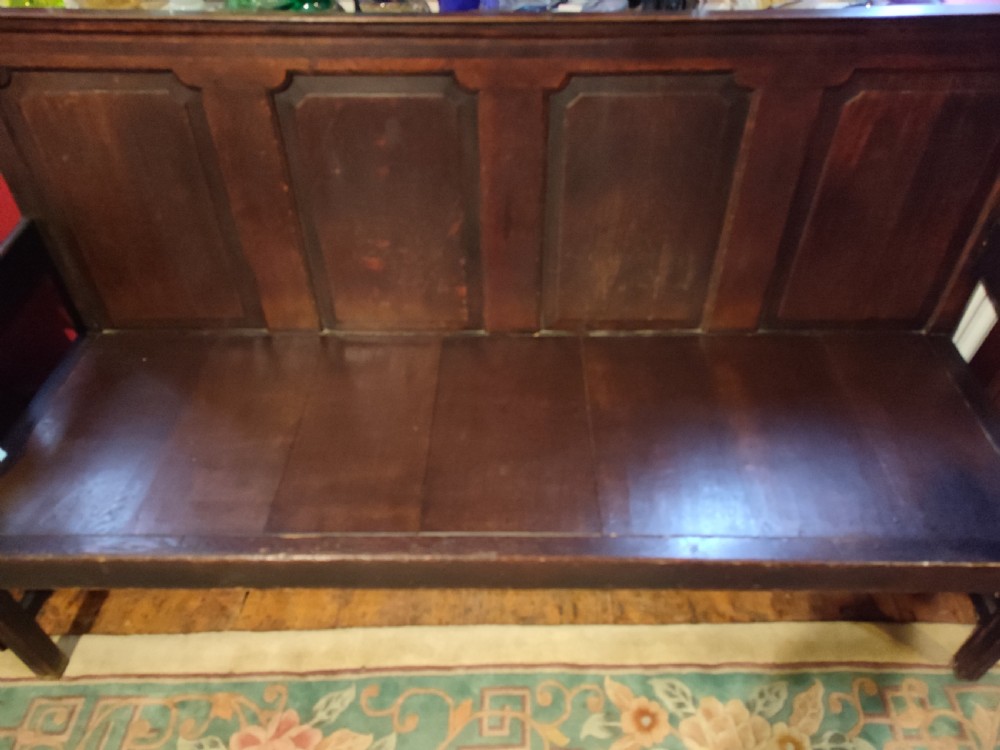 An 18th-century dark oak panelled settle with four fielded back panels and shaped side armrests. View III