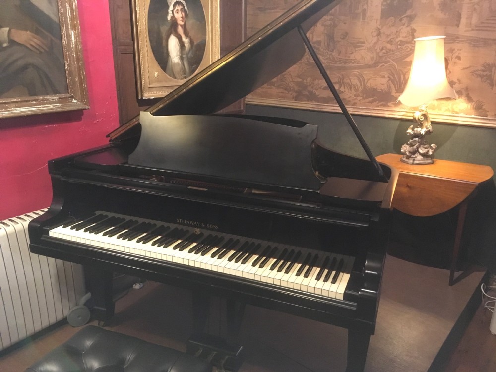 An ebonised black Steinway Model B grand piano with an open lid, full keyboard, and brass lyre pedal assembly.