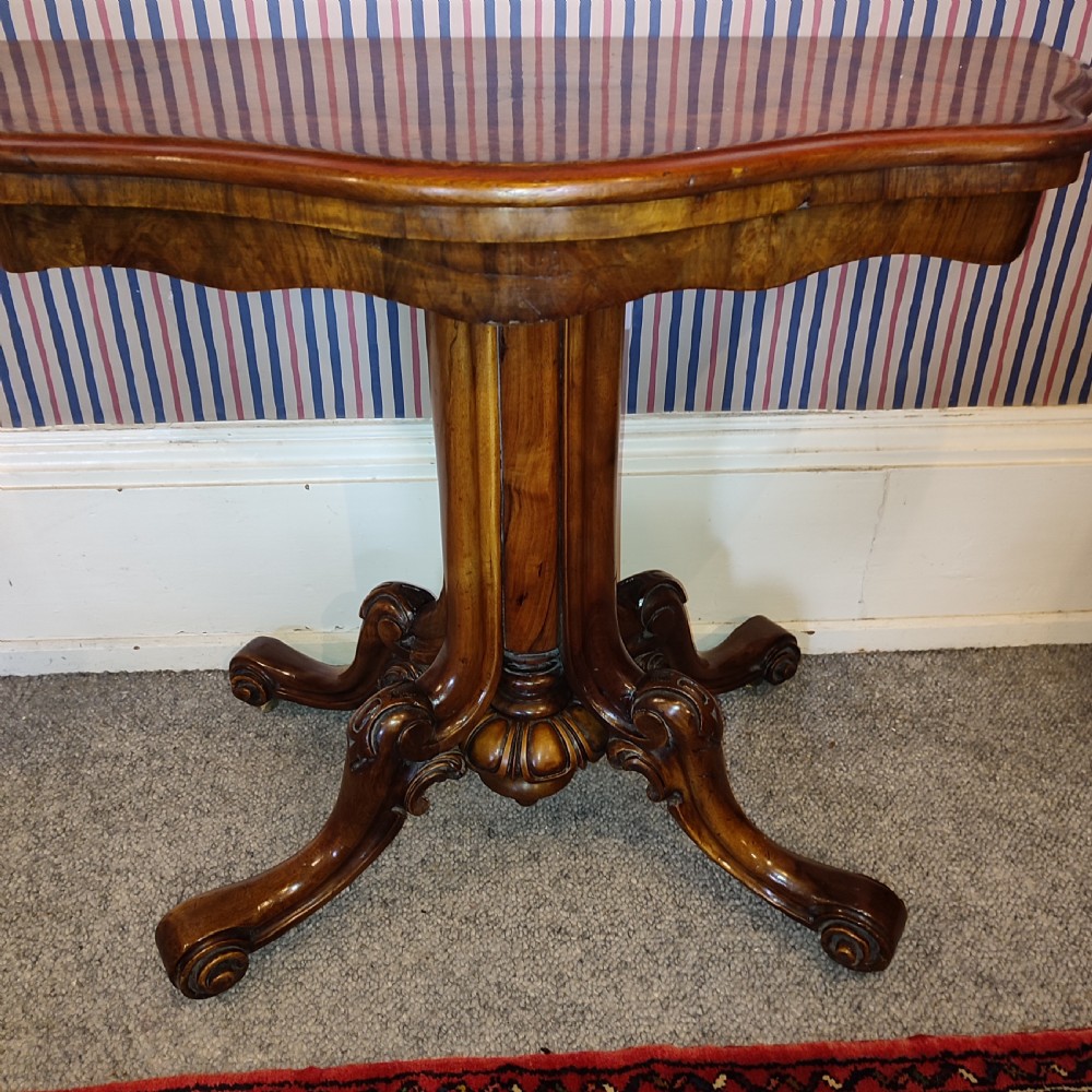 A Victorian burr walnut tea table with a serpentine fold-over top set upon a carved pedestal stem and four scrolled feet. View II