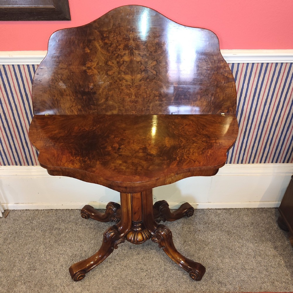 A Victorian burr walnut tea table with a serpentine fold-over top set upon a carved pedestal stem and four scrolled feet. View III