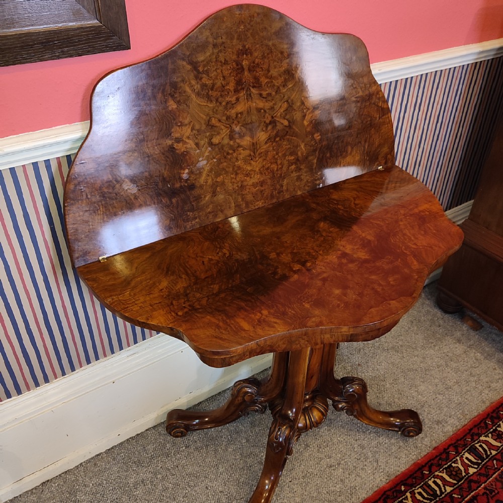 A Victorian burr walnut tea table with a serpentine fold-over top set upon a carved pedestal stem and four scrolled feet. View IV