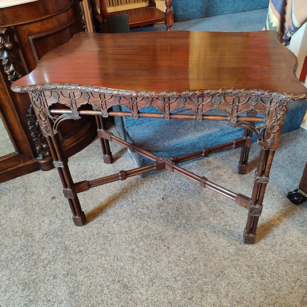 A nineteenth-century mahogany silver table crafted in the Chippendale style, featuring a shaped top, carved fretwork frieze, cluster-column legs, and an X-stretcher.