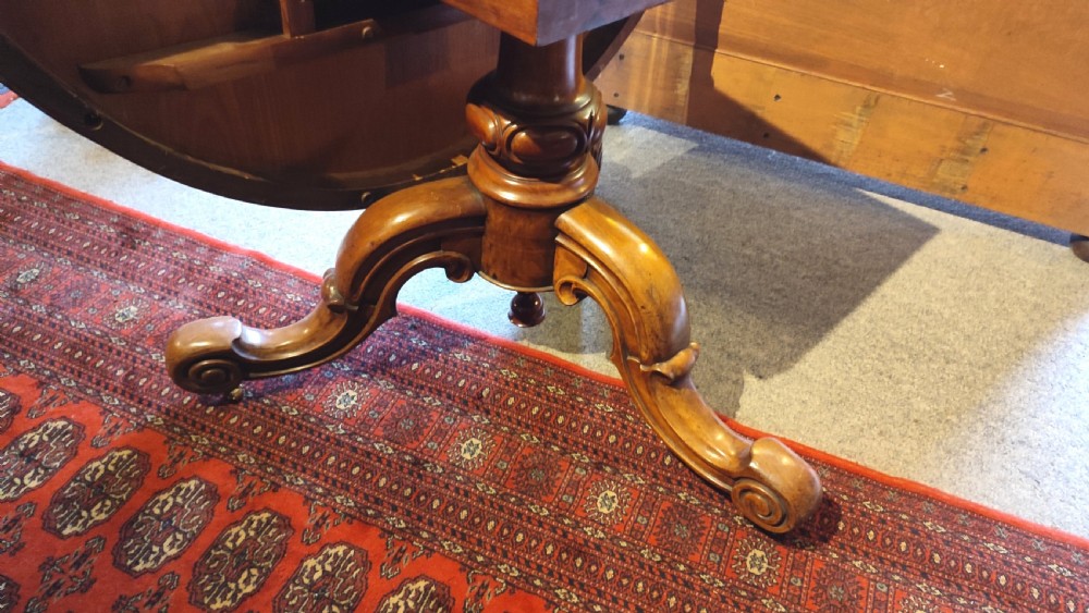 A circular Victorian burr walnut tilt-top centre table featuring floral marquetry inlay around the rim and carved scroll legs. View III