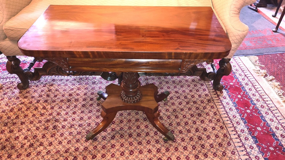 A Regency period mahogany tea table featuring a polished fold-over rectangular top set on a carved central pedestal and four splayed legs with brass castors.
