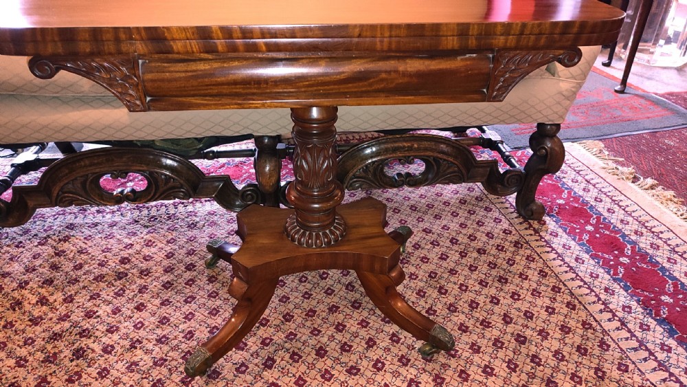 A Regency period mahogany tea table featuring a polished fold-over rectangular top set on a carved central pedestal and four splayed legs with brass castors. View II