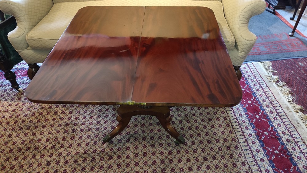 A Regency period mahogany tea table featuring a polished fold-over rectangular top set on a carved central pedestal and four splayed legs with brass castors. View III