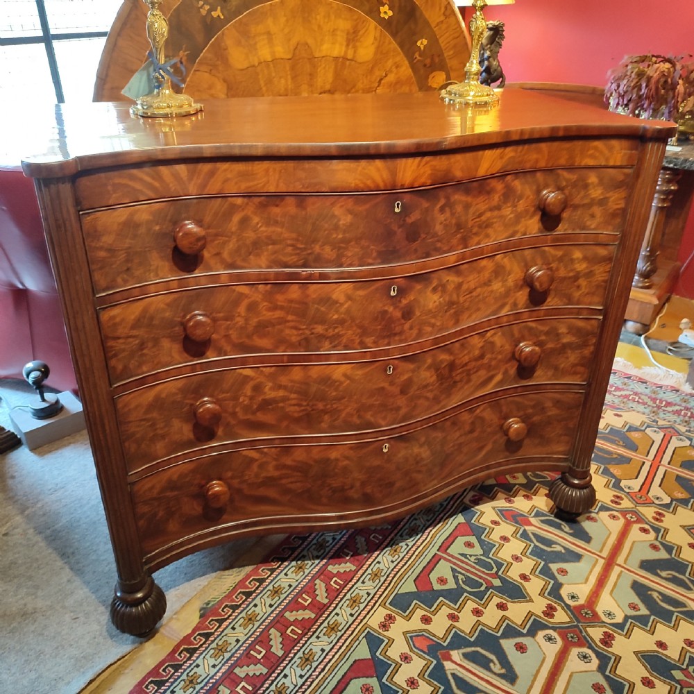 A William IV flame mahogany chest featuring four graduated serpentine drawers with reeded side columns and turned lobed feet.