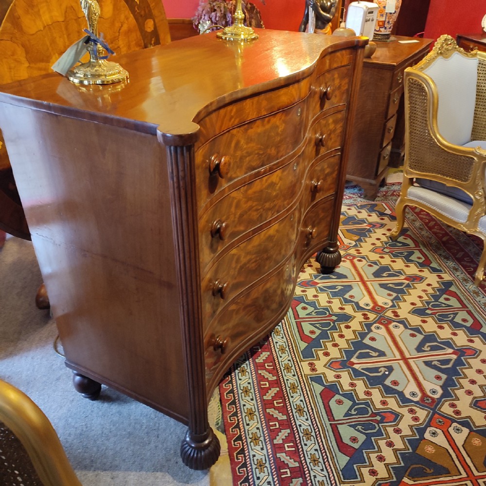 A William IV flame mahogany chest featuring four graduated serpentine drawers with reeded side columns and turned lobed feet. View II