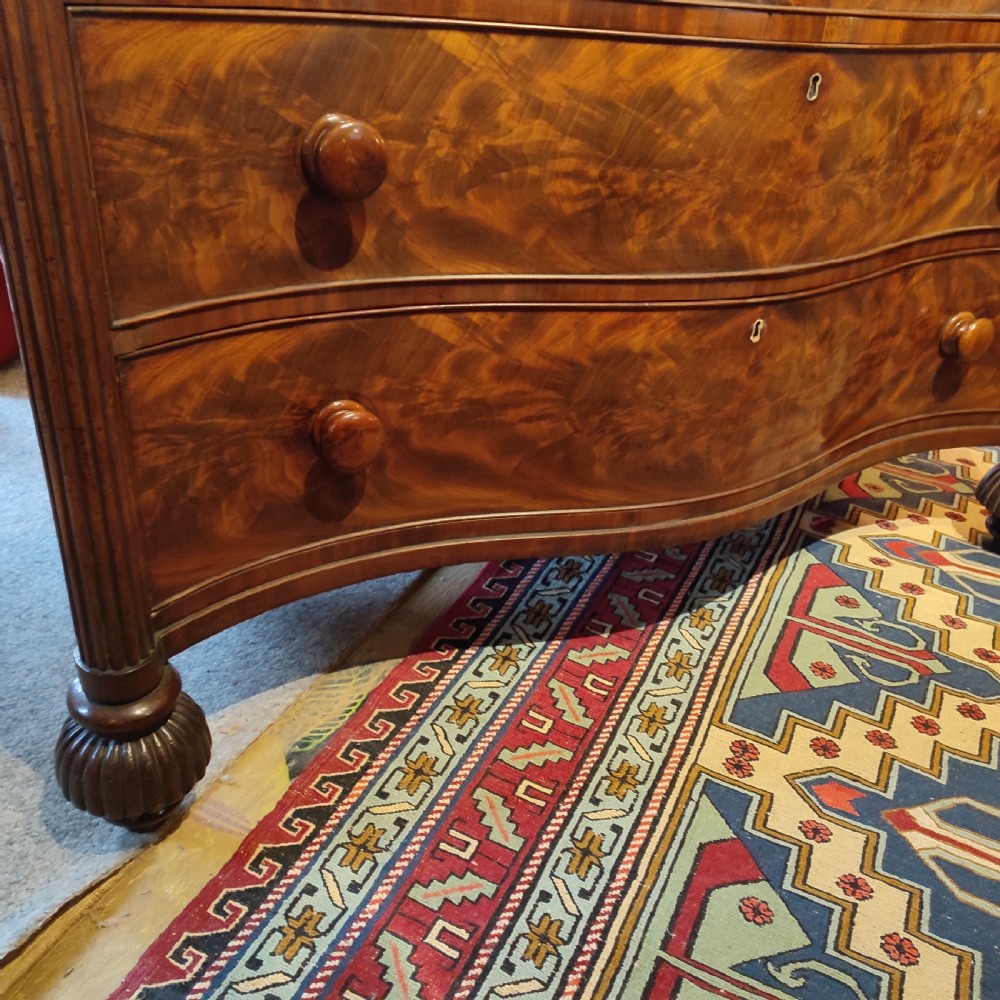 A William IV flame mahogany chest featuring four graduated serpentine drawers with reeded side columns and turned lobed feet. View III