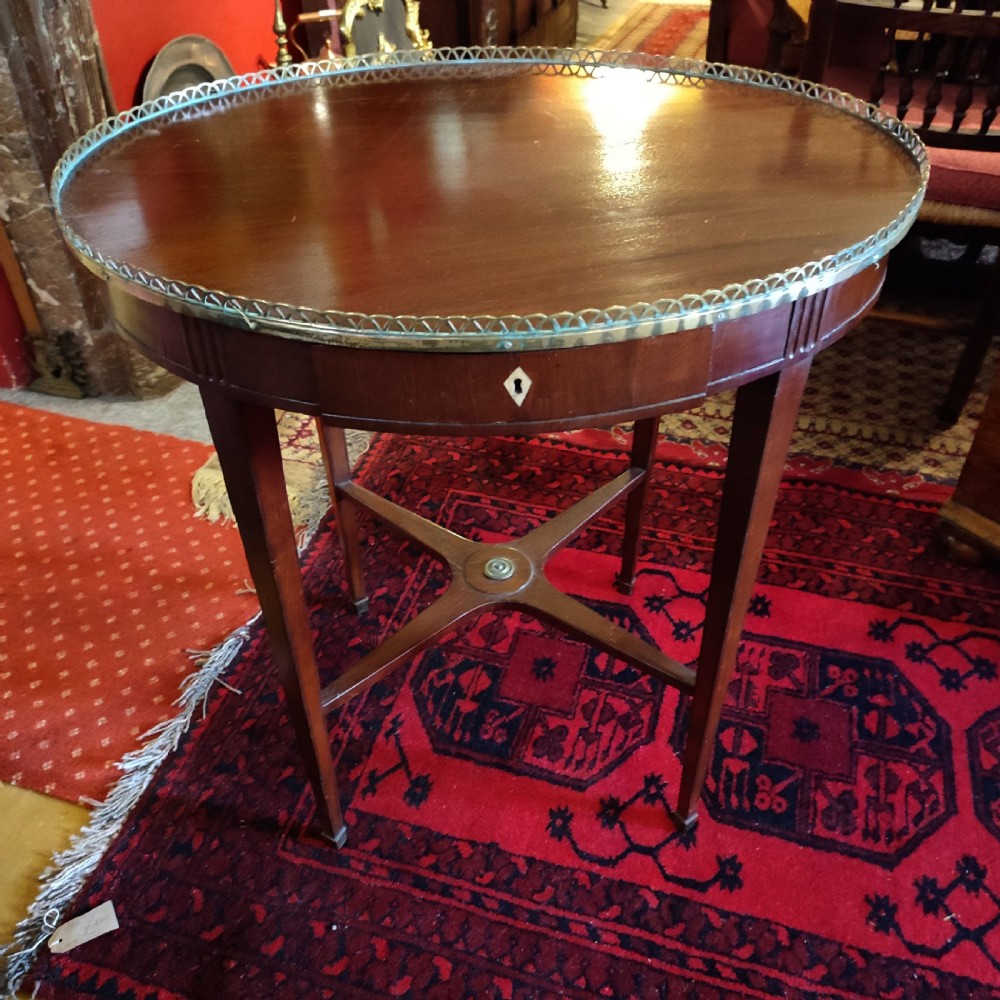 An 18th-century George III oval mahogany occasional table featuring a pierced brass gallery rim, single drawer, square tapered legs, and an X-form stretcher.