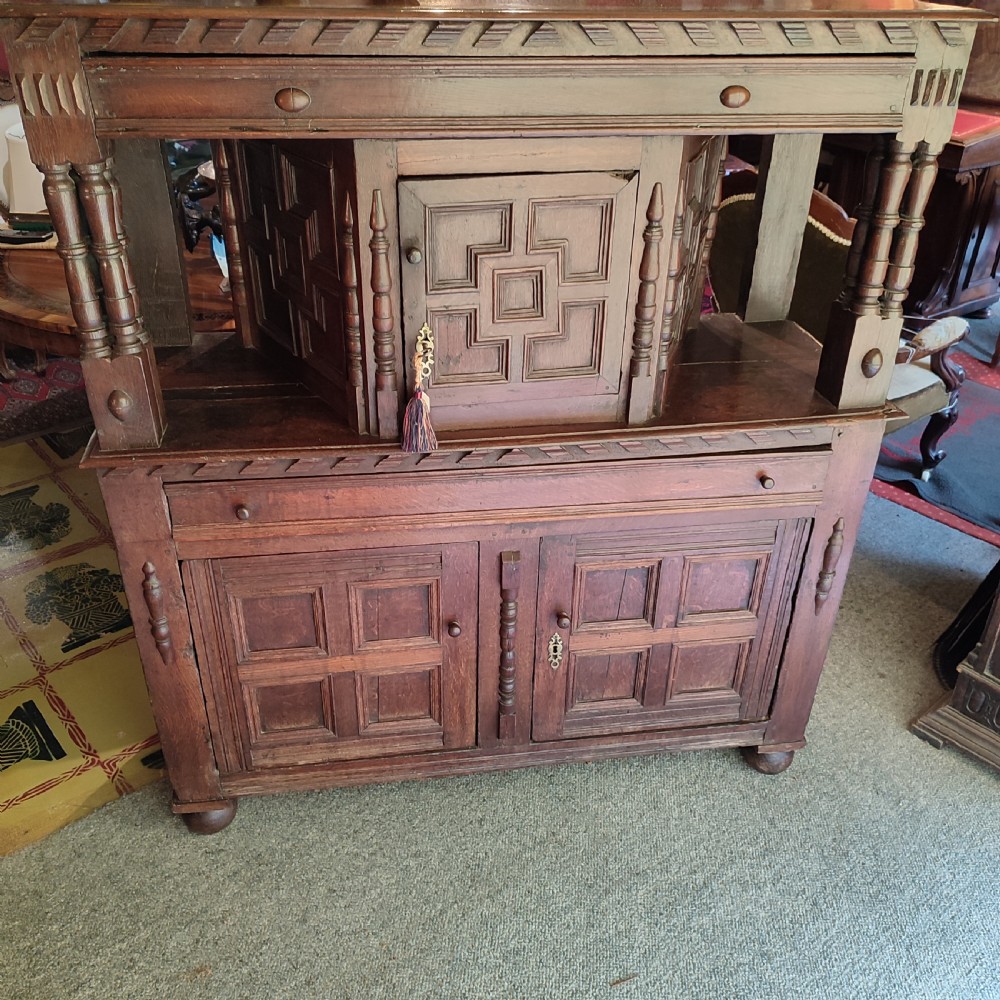A late 17th-century dark oak court cupboard featuring geometric panel doors and turned baluster supports.