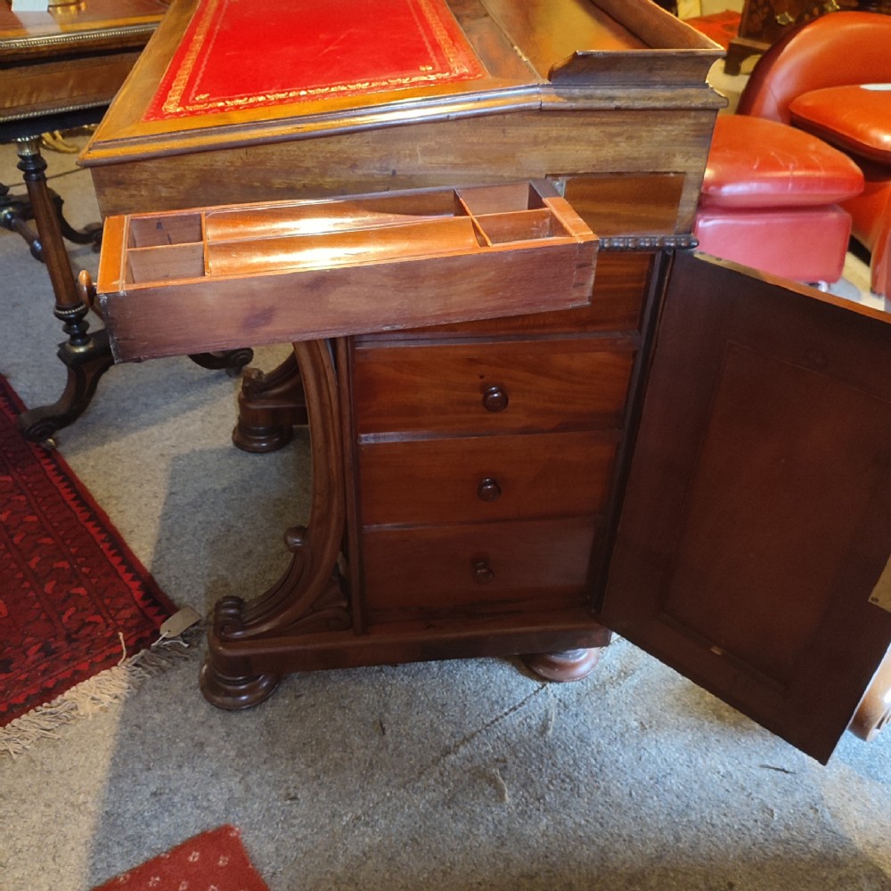 A Regency mahogany davenport desk featuring a red leather-lined sloped writing top, carved scroll supports, and beaded edging. View IV